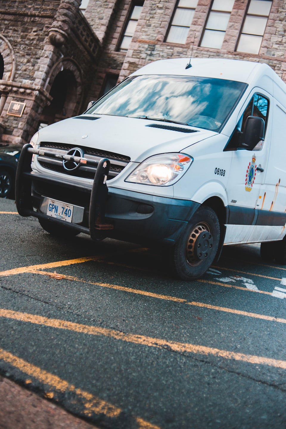 Valge Mercedes-Benz Sprinter kaubik pargitud kivimaja ette.