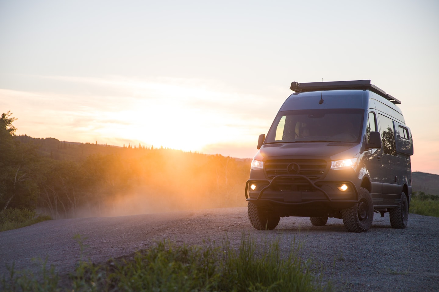 Hall Mercedes-Benz Sprinter matkaauto pargitud tolmusele teele päikeseloojangul.